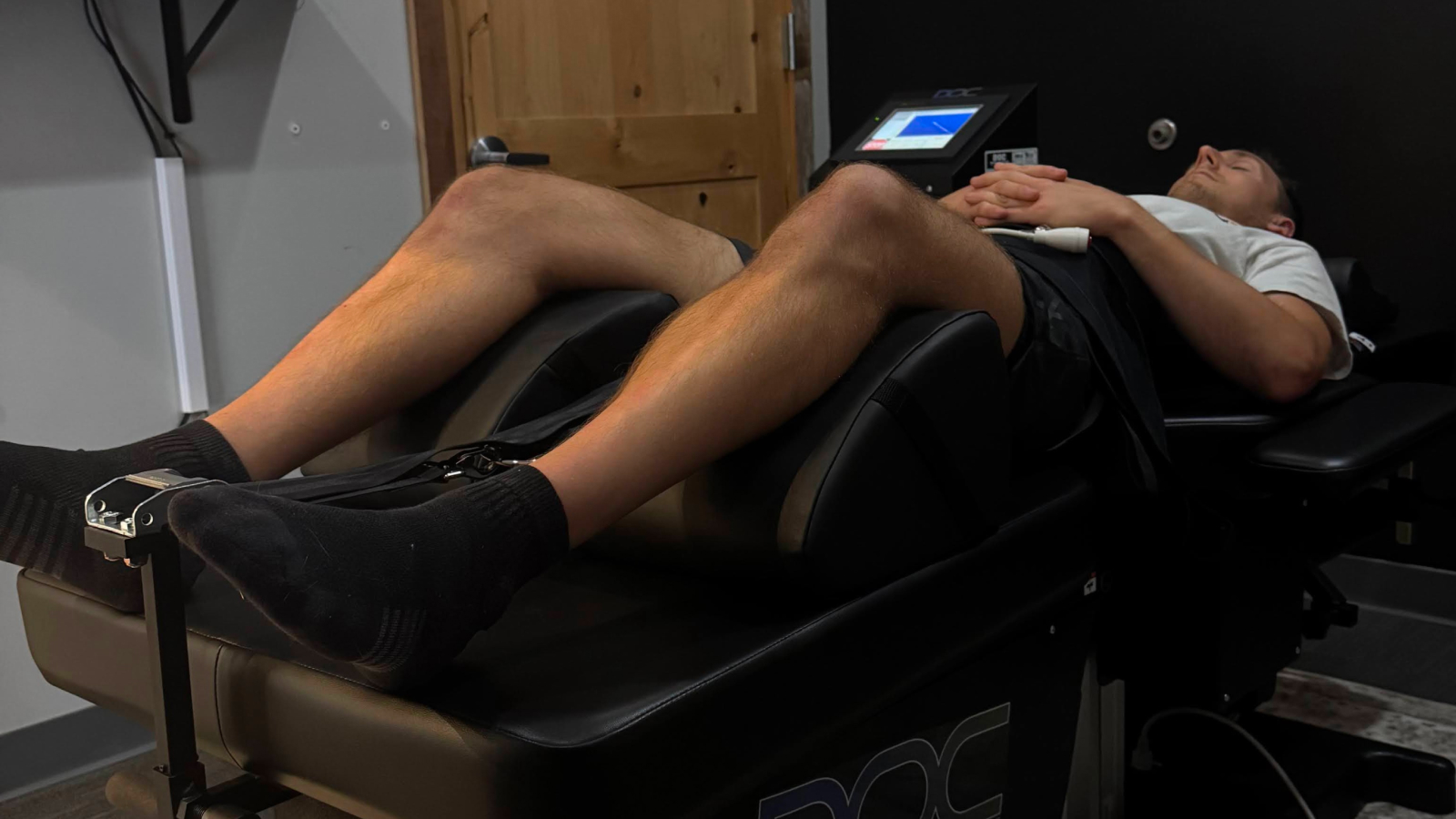 `Patient lying relaxed on a DOC spinal decompression table during a treatment session at Elite Wellness Chiropractic, with the decompression unit's control screen visible in the background`