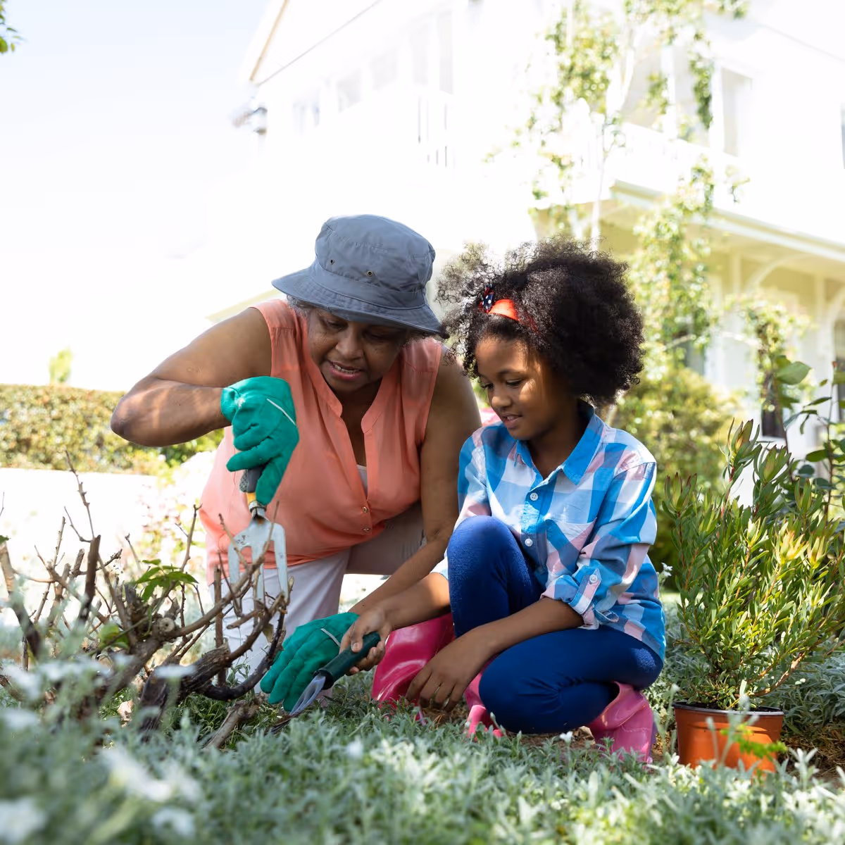 Nurturing growth, one step at a time. Adult helping a child trim plants in a sunny garden.