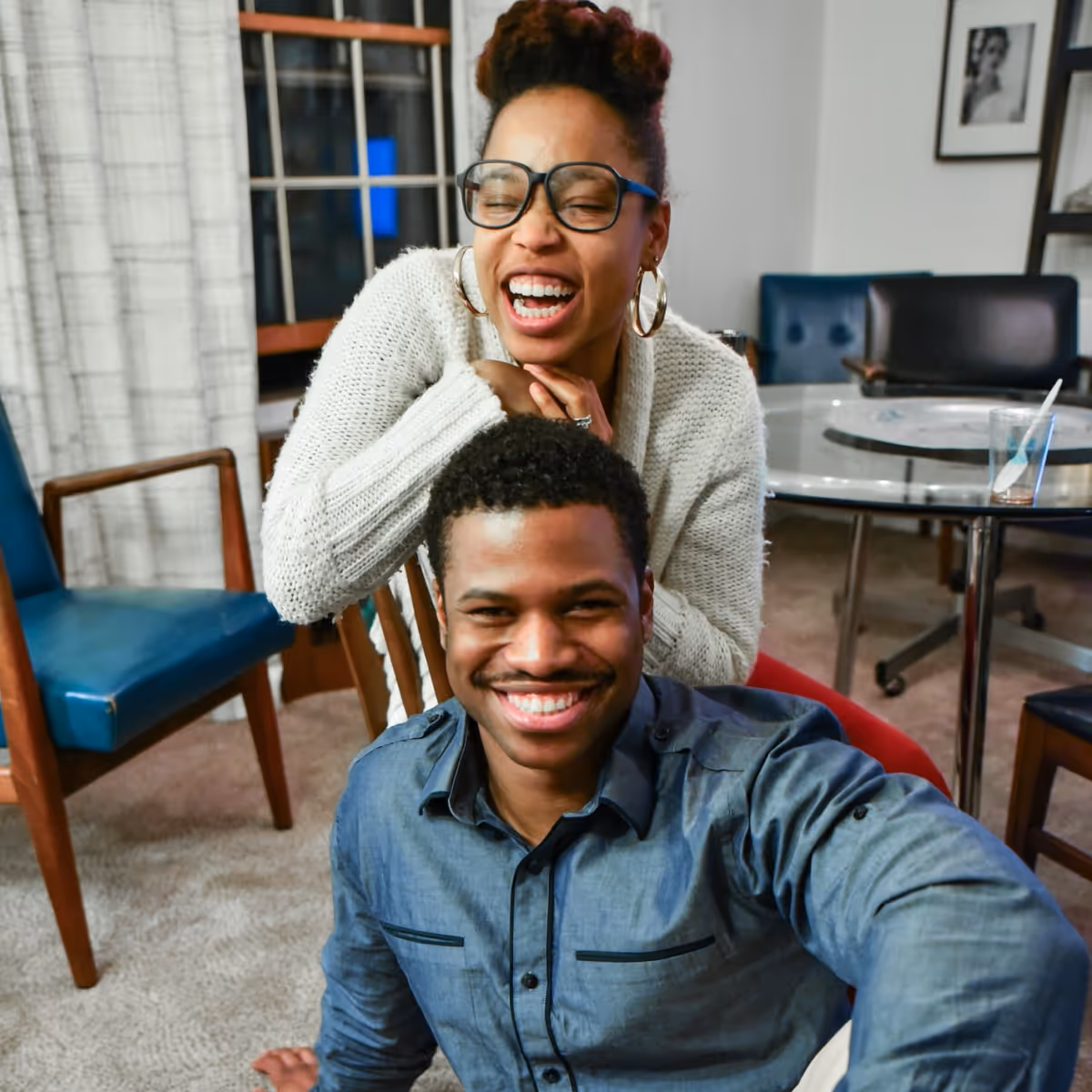 Home should feel like joy. Two people laughing together in a cozy living room, enjoying a relaxed evening at home.