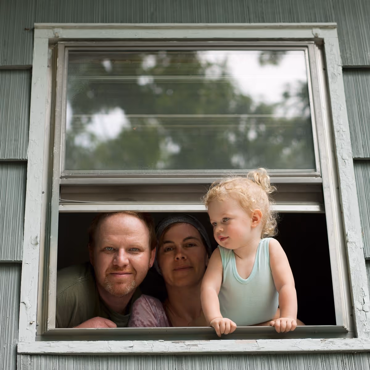 A welcoming place to call home. Family looking out an open window, smiling together.