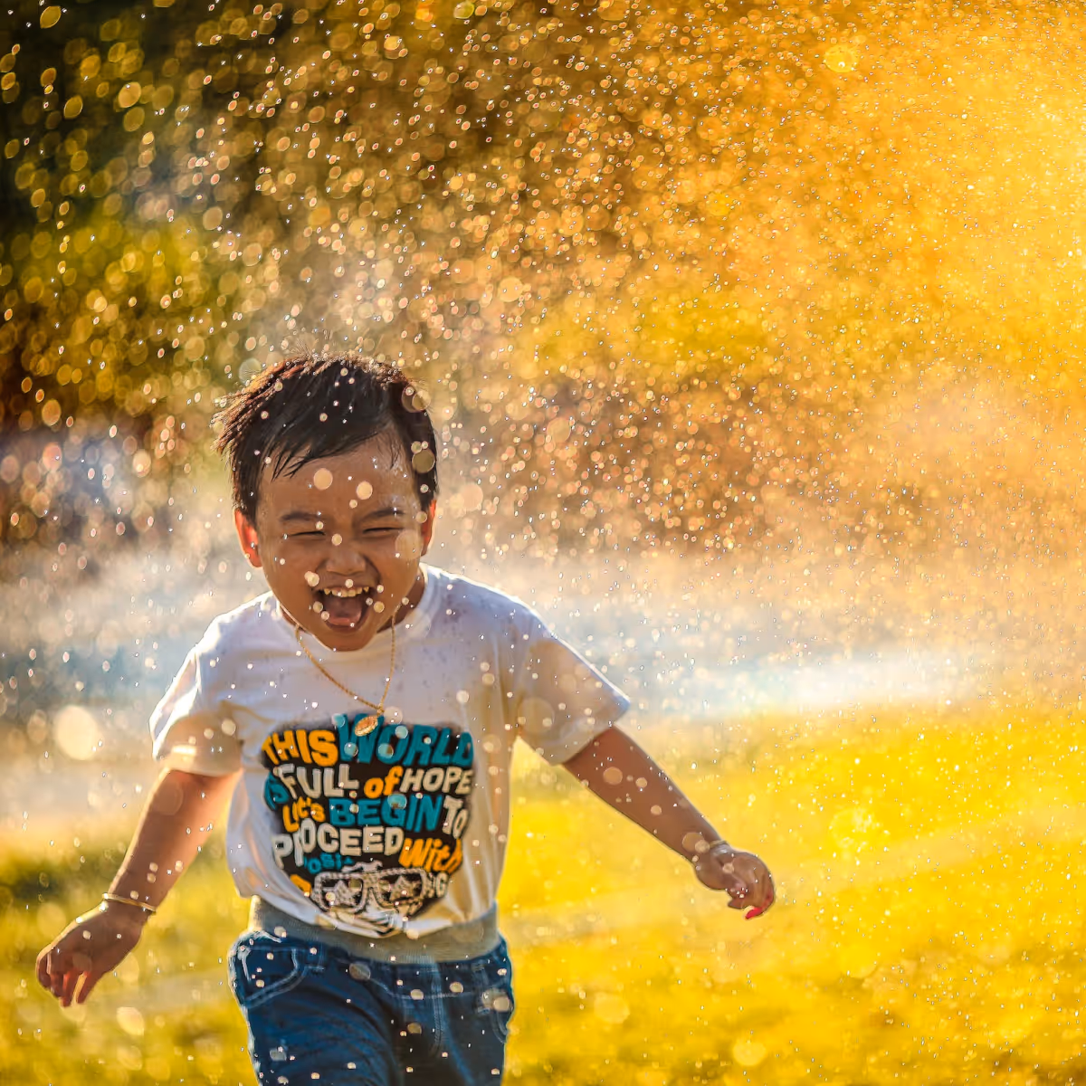 Freedom and joy start with a good home. One child running through the sprinklers of a grassy field at sunset.