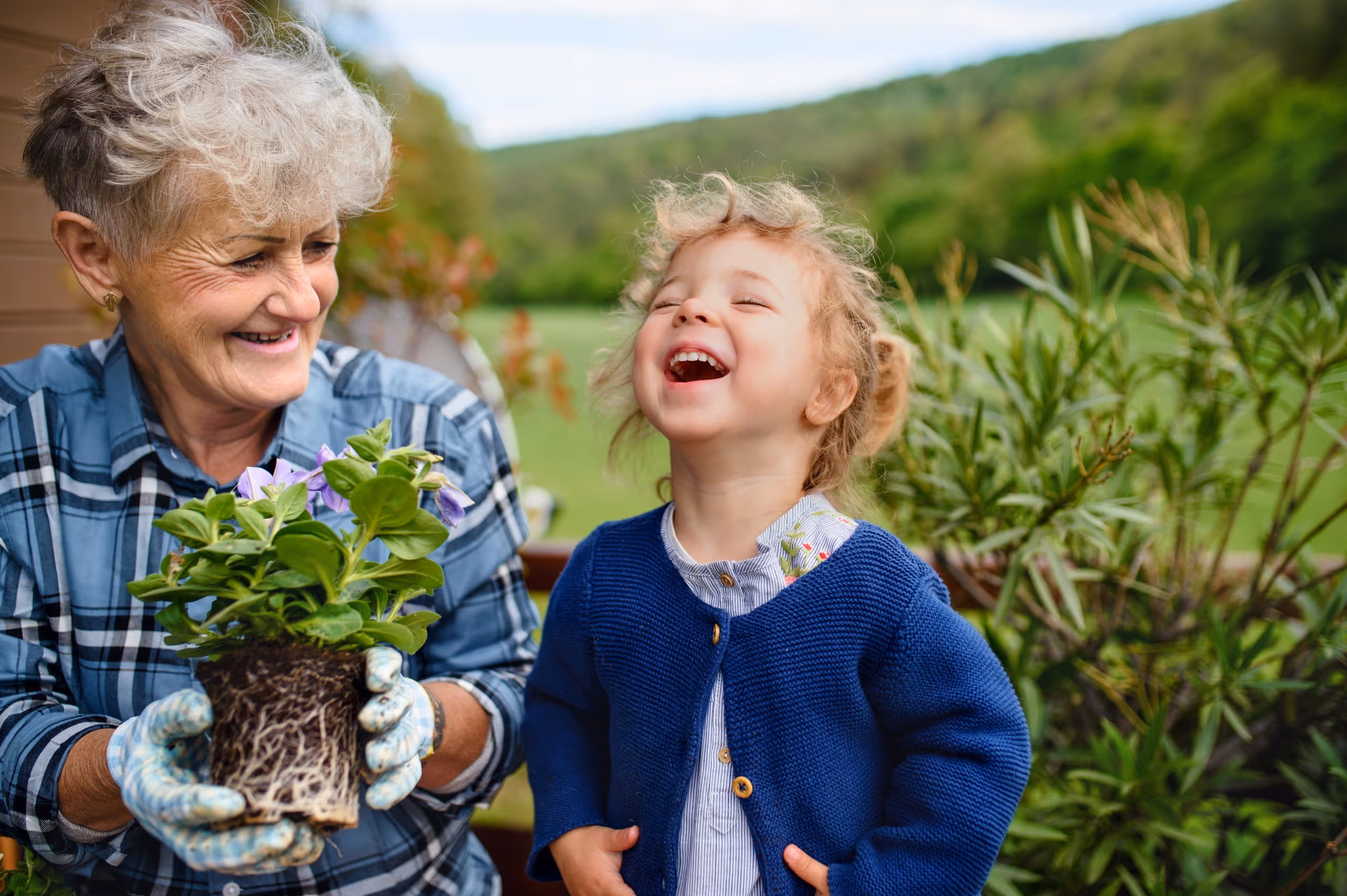 Joy blooms when we care for what we grow. Adult and child smiling together while holding a potted flower.
