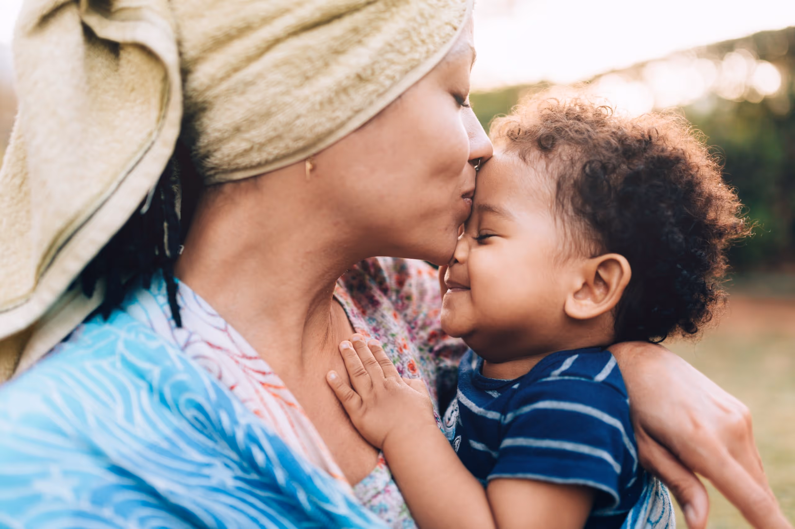 The small moments make a home. Parent kissing a baby’s cheek while sitting outside.