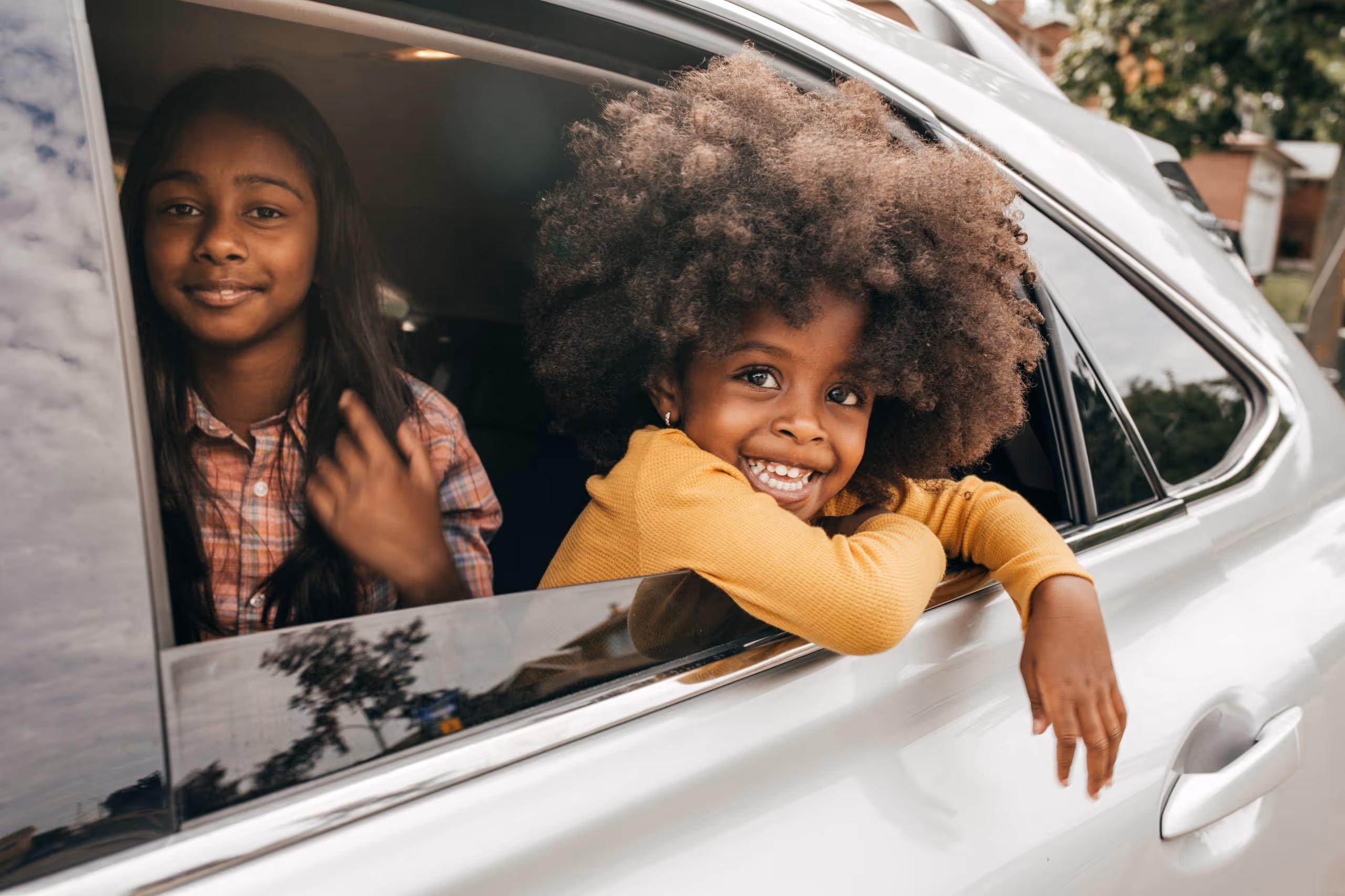 Our focus is on people, not paperwork. Two kids smiling through an open car window during a sunny day.