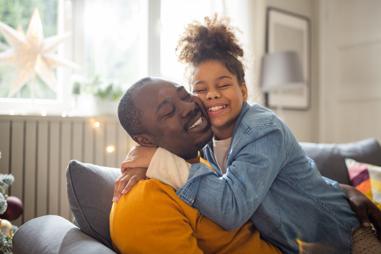 Belonging starts at home. Parent and child hugging and smiling together in a cozy living room.