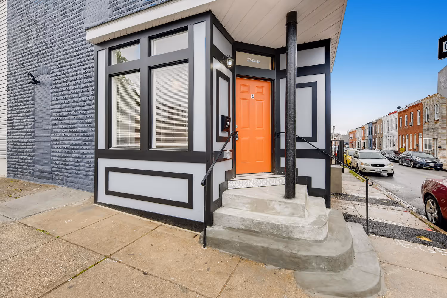 Distinctive homes with local charm. Exterior view of a Baltimore row home with grey and black trim and an orange door.