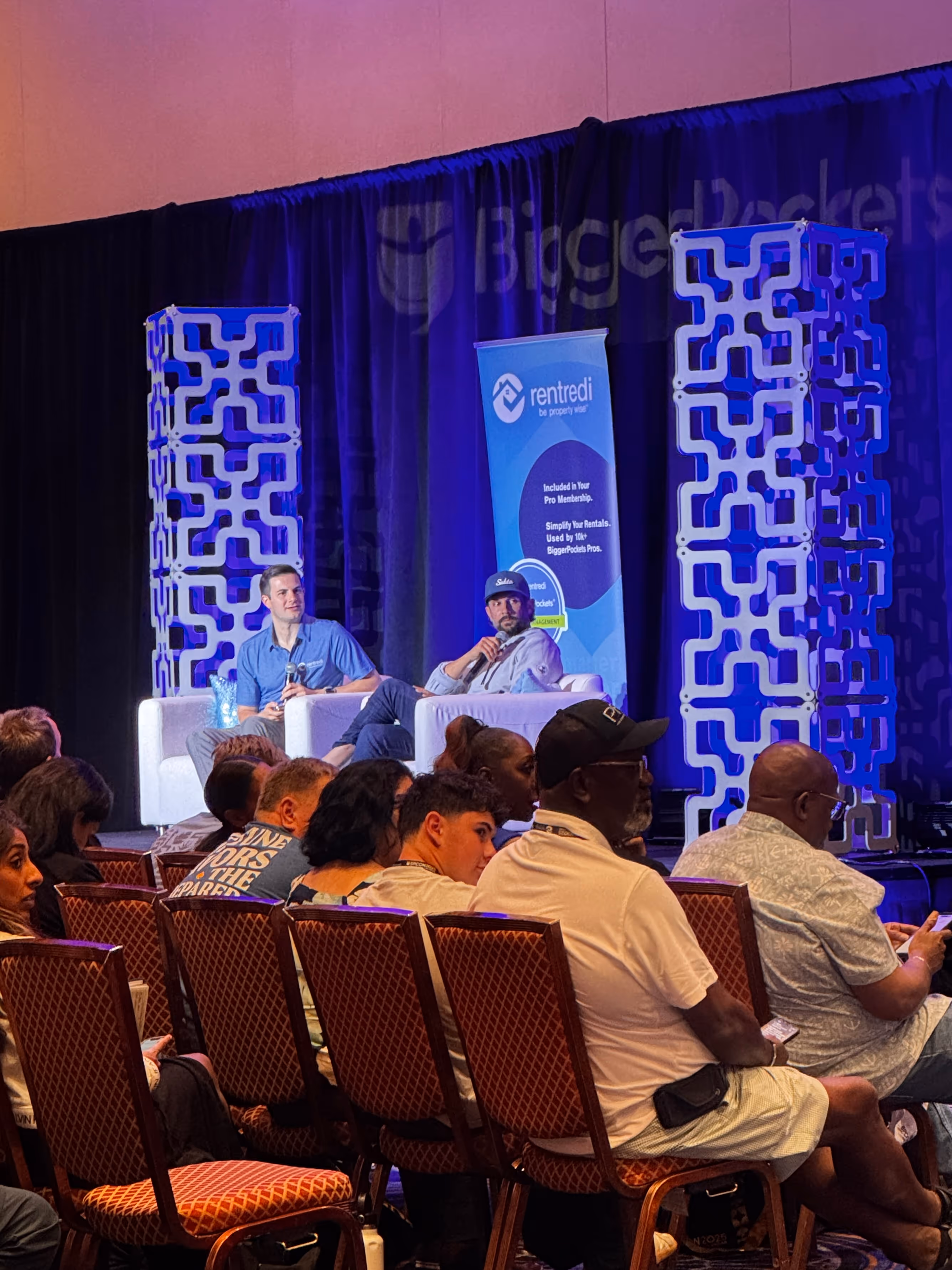 Pace Morby and RentRedi representatives sit on stage in white chairs during the BPCON panel discussion, "AI & Creative Financing," in front of a seated audience. The stage has geometric blue decor and a "RentRedi" banner, with "BiggerPockets" partly visible on the backdrop.