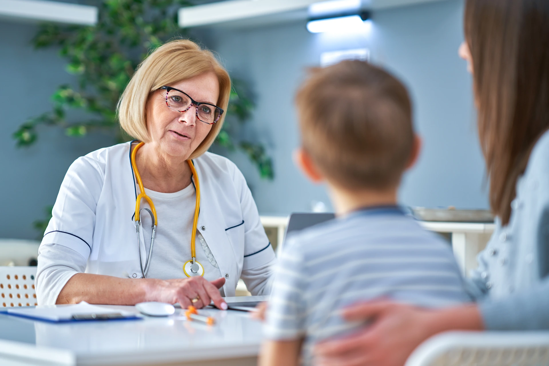 Doctor talks with a young patient and parent in a clinic exam room.