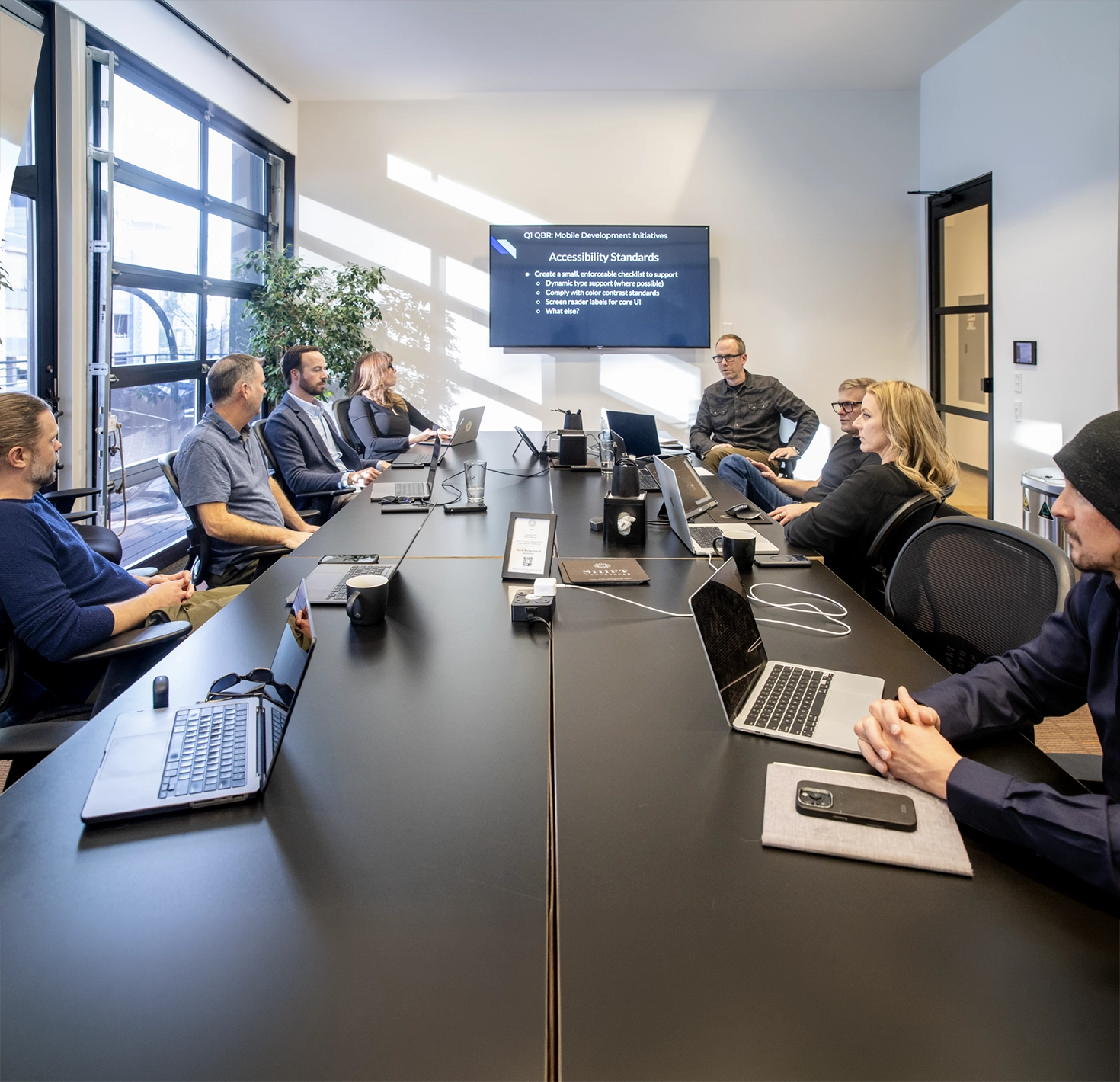 The 303 Software team gathered around a conference table with laptops during a presentation on web accessibility standards.