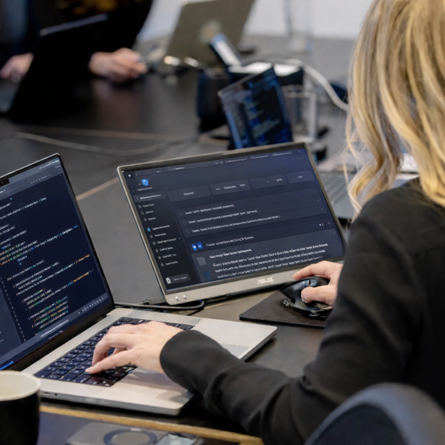 303 Software developer working across a code editor and an AI tool interface on a dual-laptop setup while integrating AI into a client application.