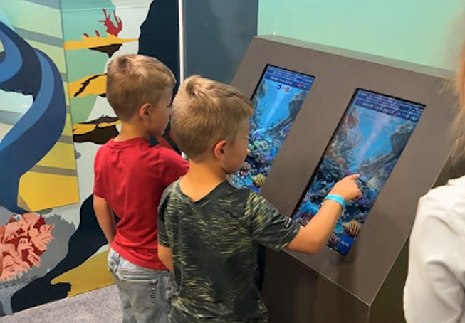 Kids playing an interactive DNA and genetics learning game at Butterfly Pavilion's Origins: Building Life exhibit