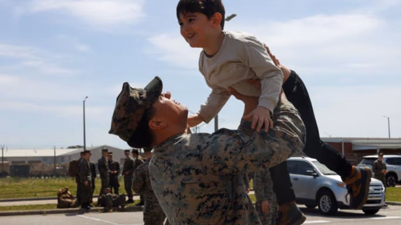 A man in a military uniform is holding a young boy in the air.