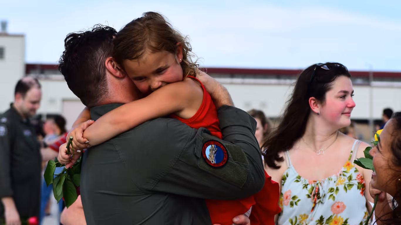 A man in a military uniform hugs a little girl.