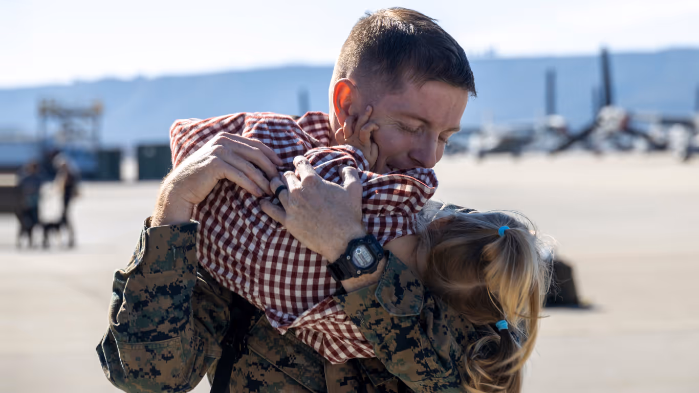 A man in a military uniform hugs a little girl.