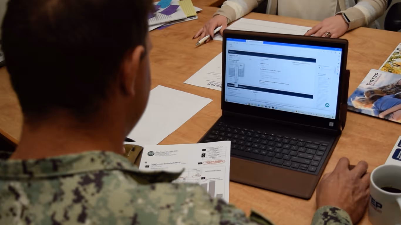 A man in a military uniform is looking at a laptop.