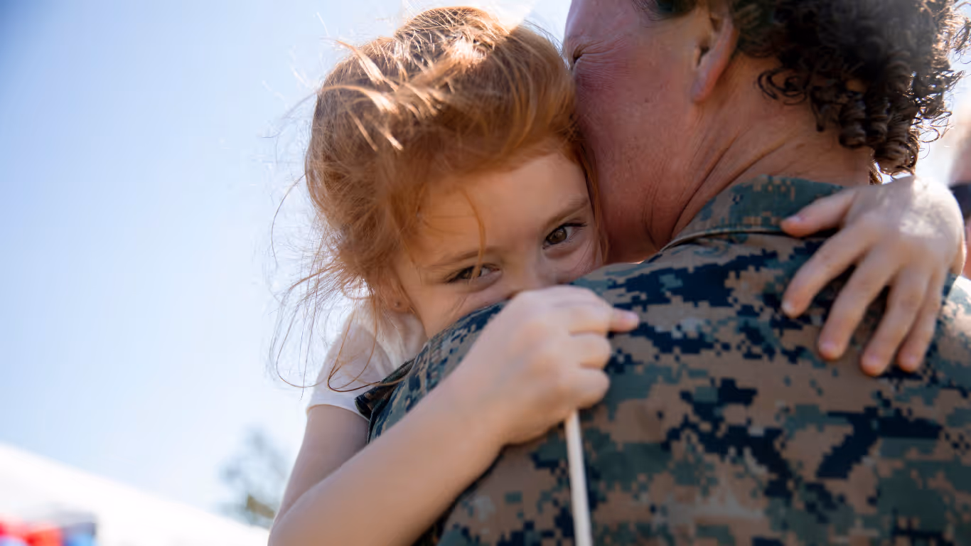 A little girl hugging a man in camouflage.