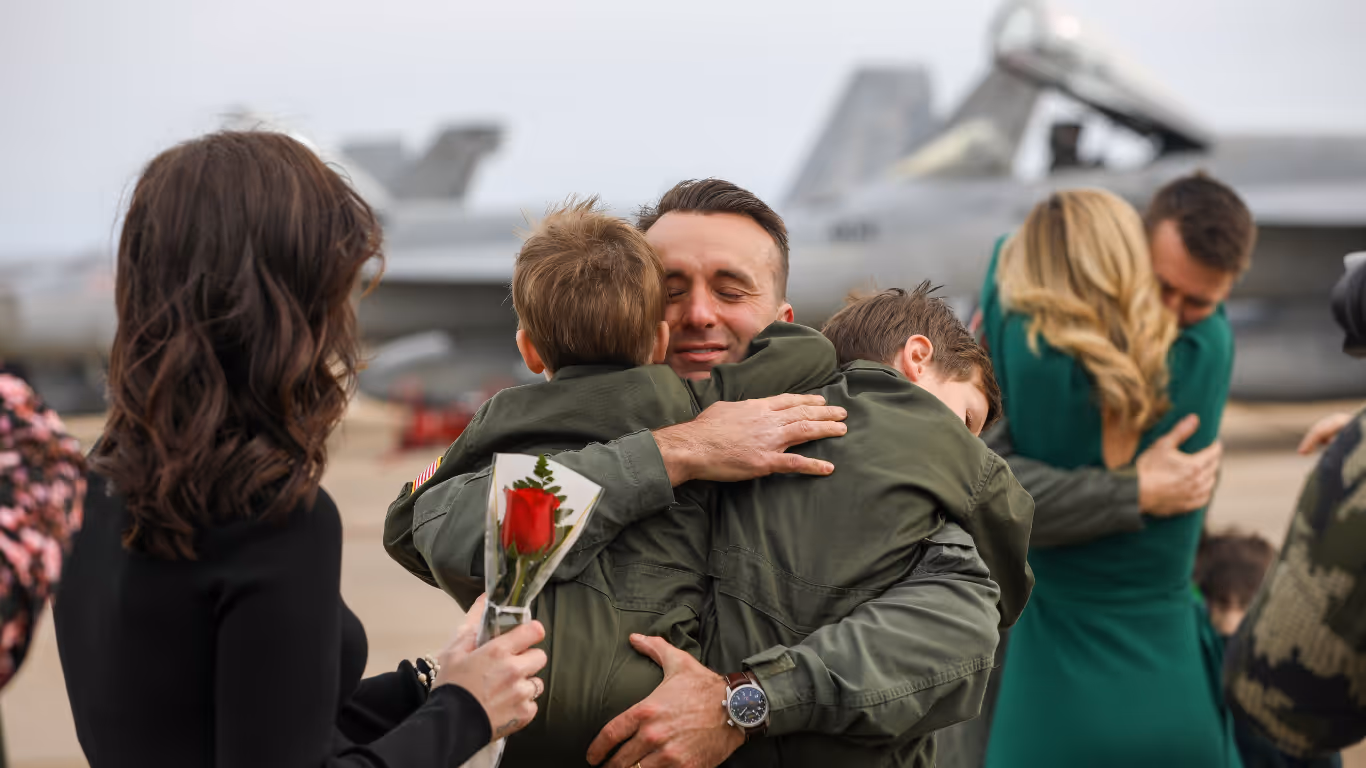 A man in a military uniform hugs a young boy.