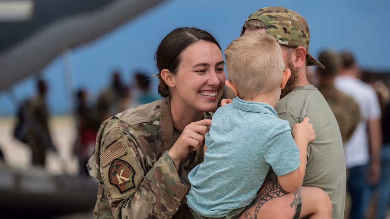 A woman in army fatigues hugs a young boy.