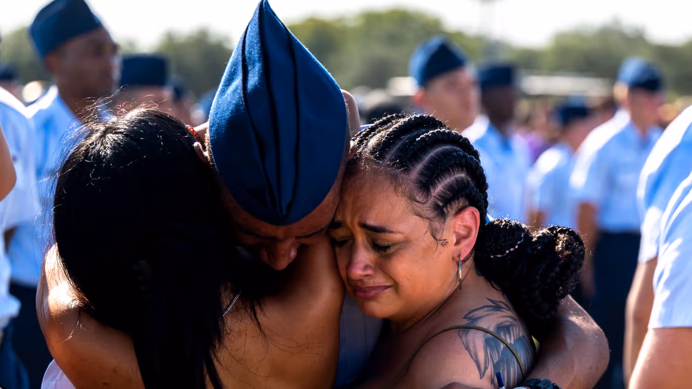 A woman with a tattooed arm hugs a man in a military uniform.