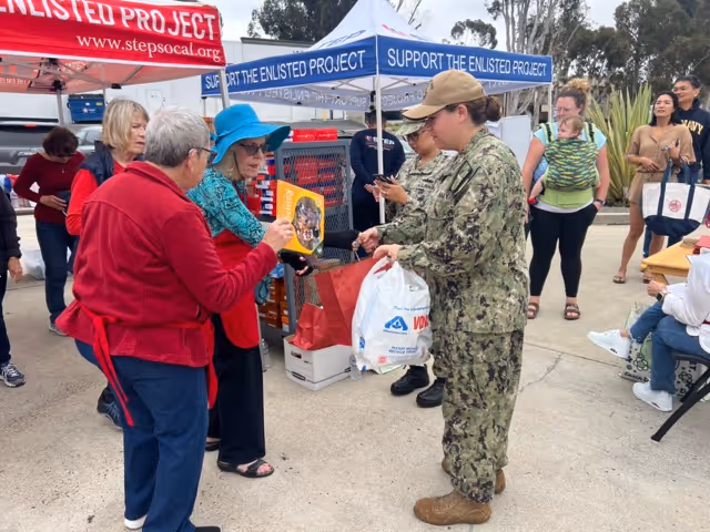 A woman in a red jacket is handing a book to a woman in a military uniform.