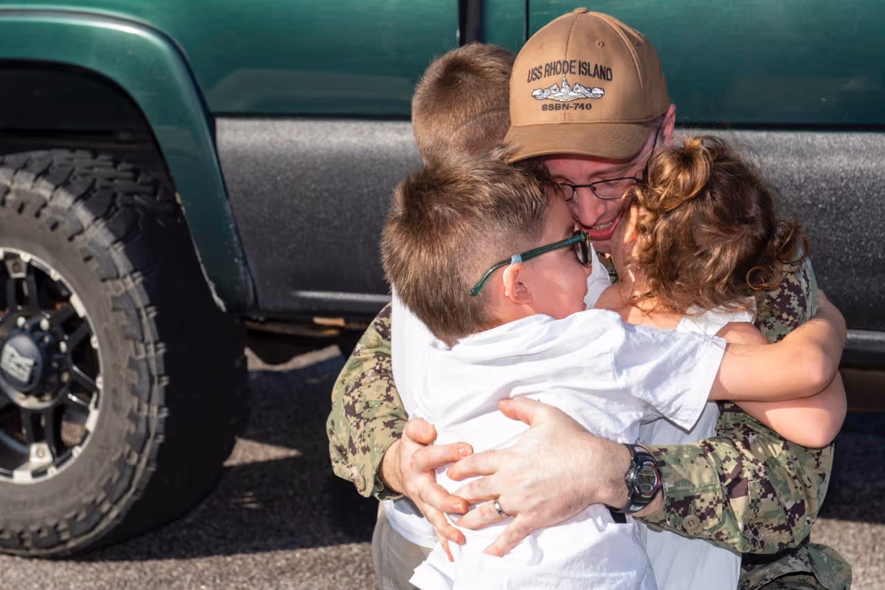 A man in a camouflage hat hugs a young boy.