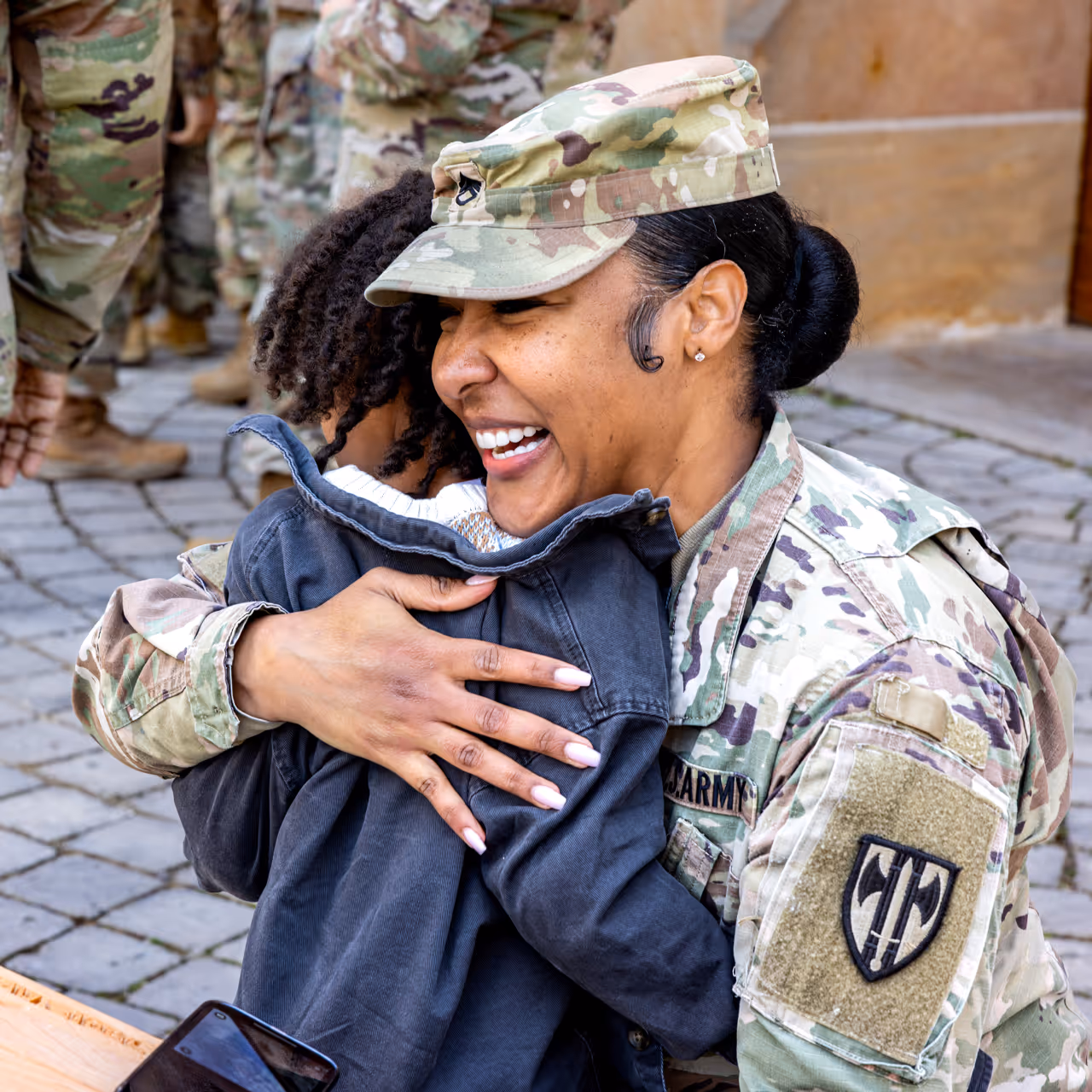 A woman in a military uniform hugs a child.