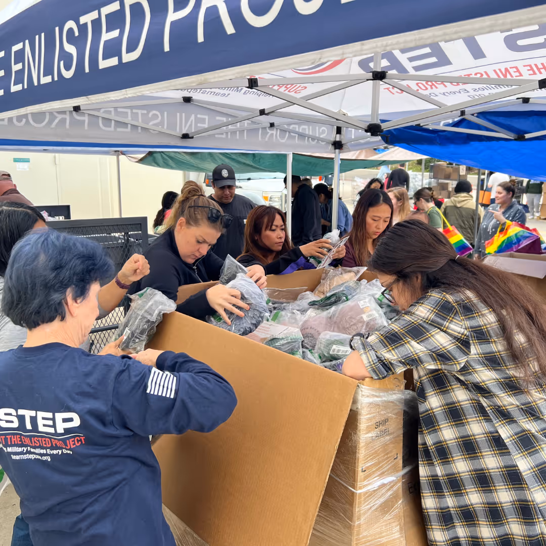 A woman in a blue shirt is reaching into a box of items.