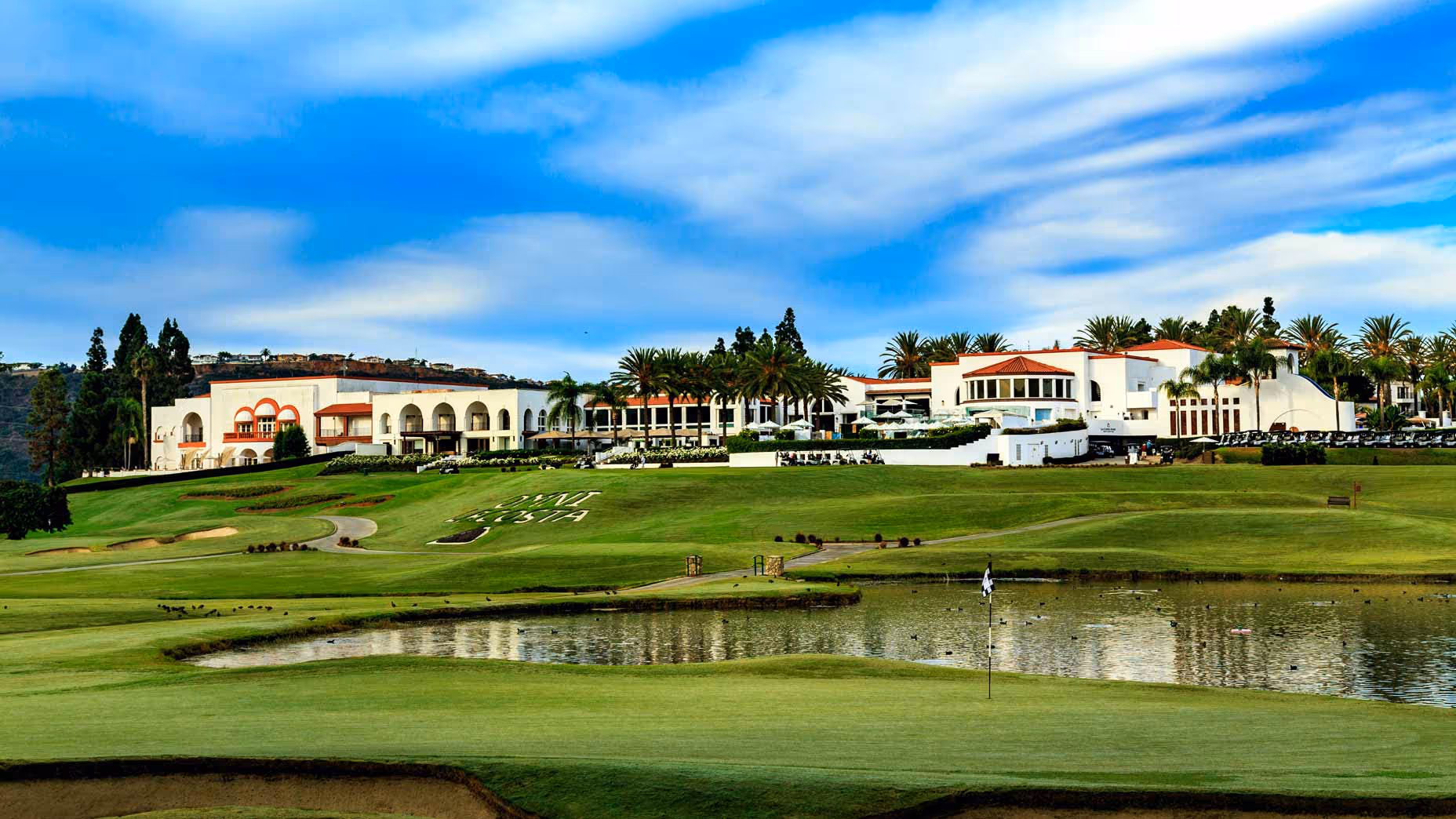 A golf course with a lake and a building in the background.