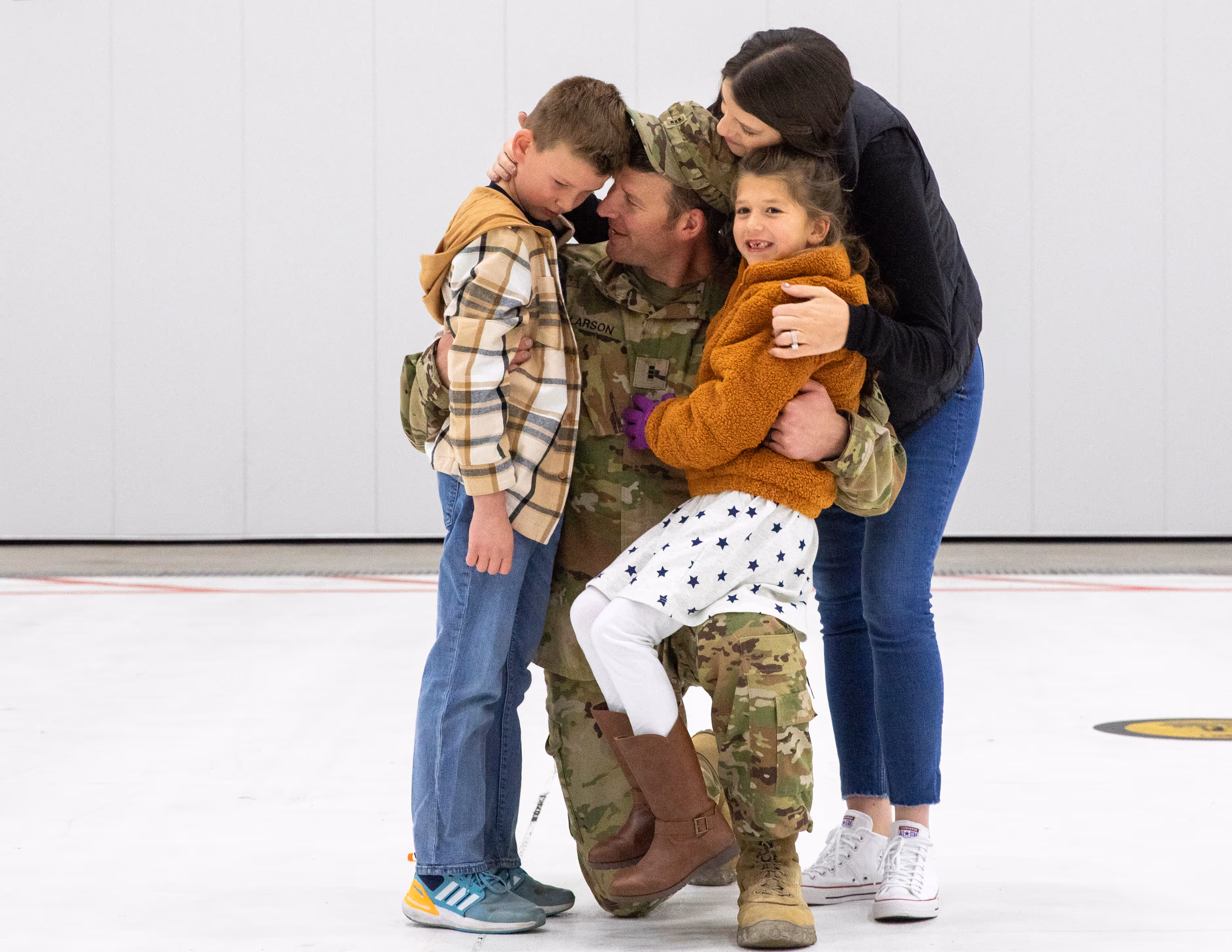 A man in army fatigues hugs a little girl.