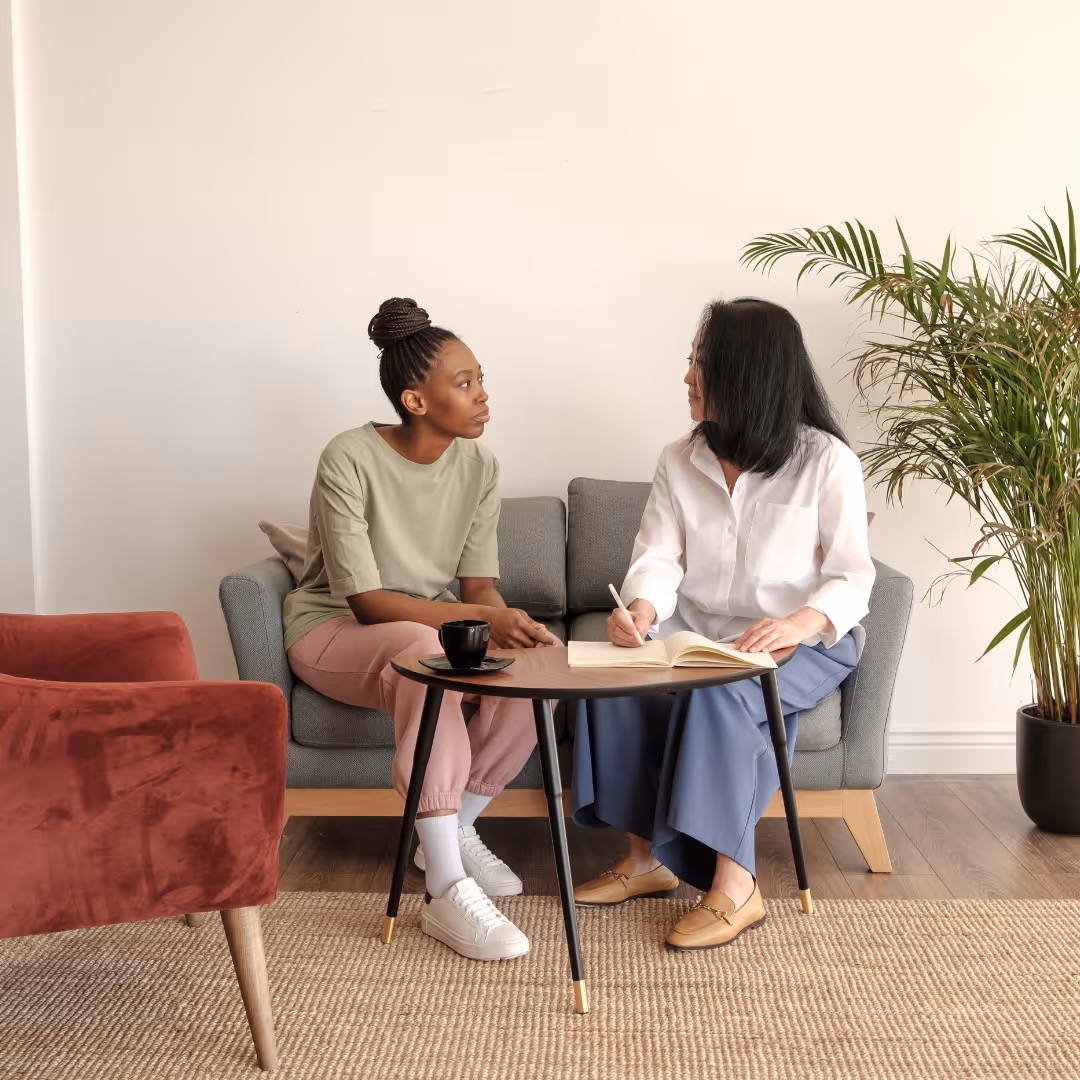 Two women sitting on a couch talking.