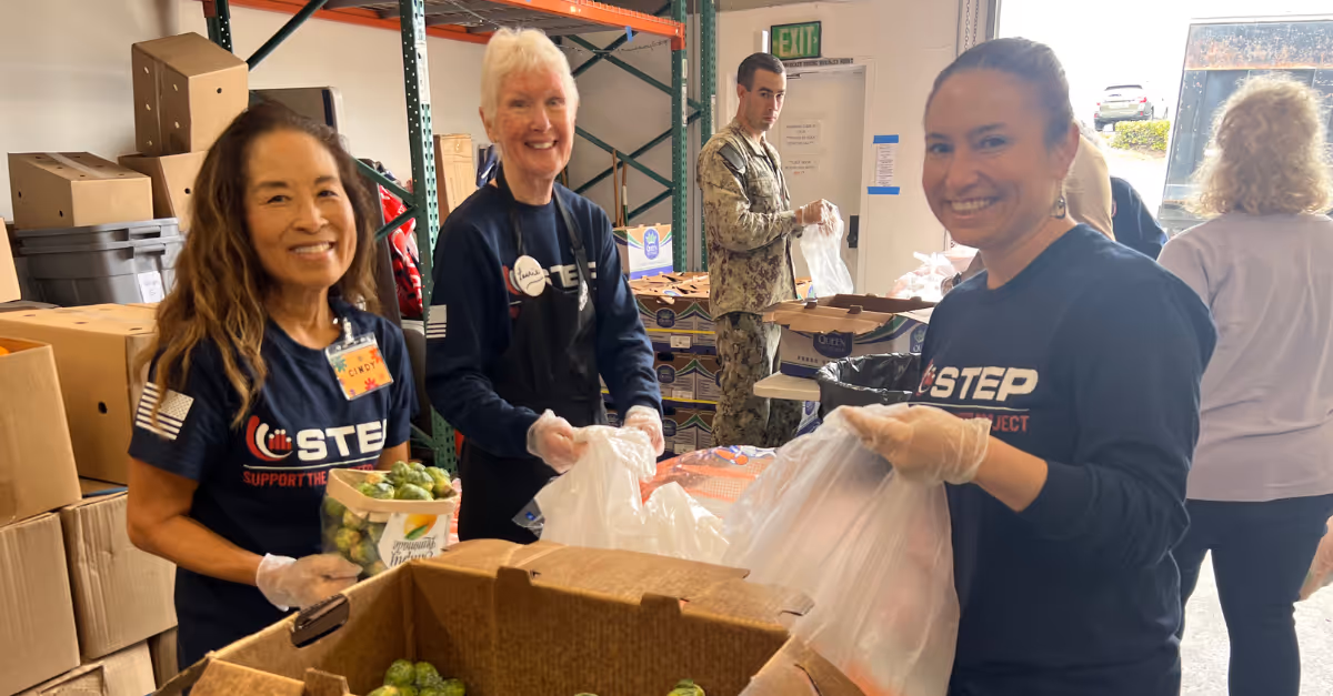 Two women are smiling and holding bags of food.