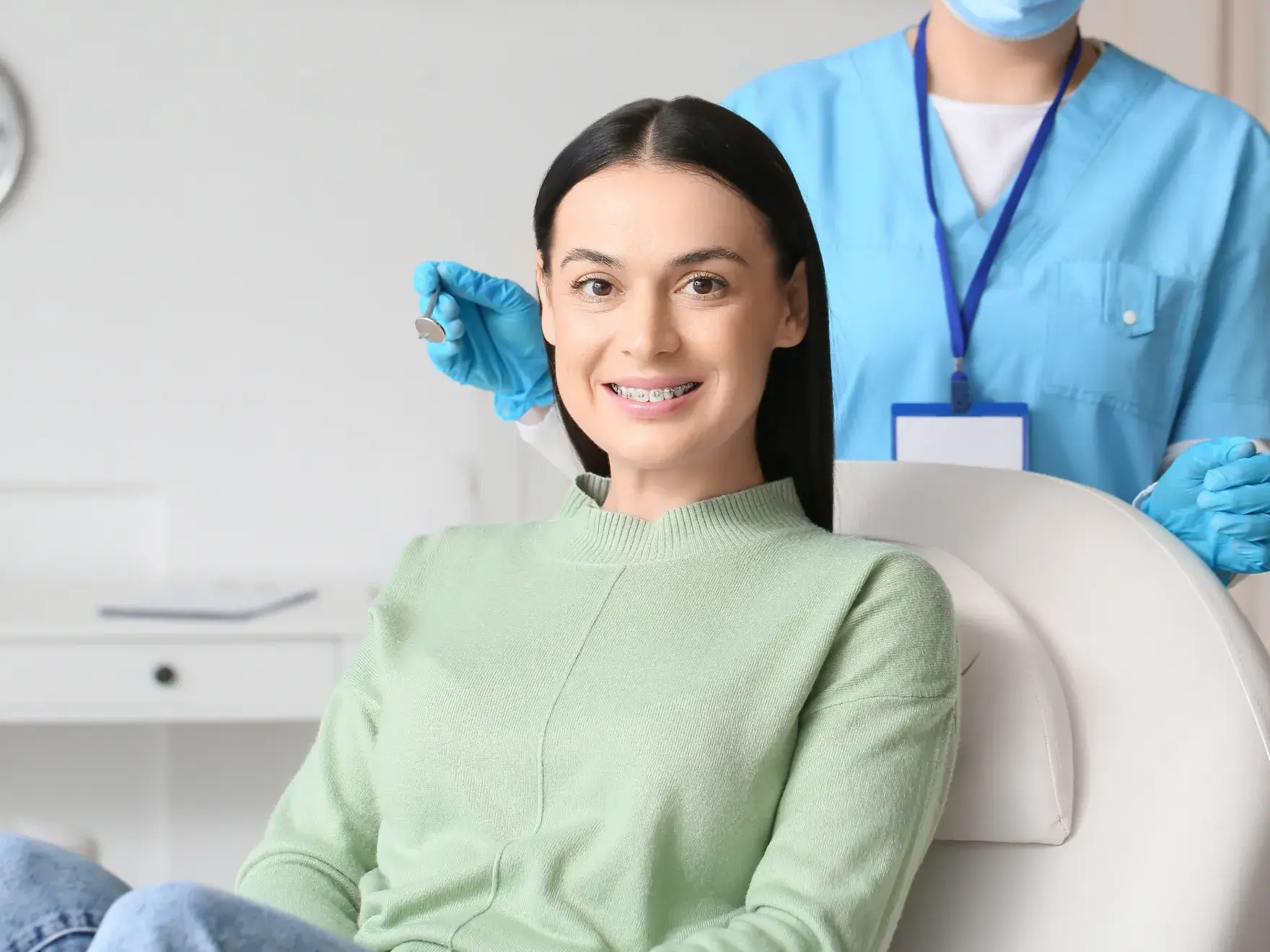 A woman with braces sits in a dental chair while a dentist stands behind her.