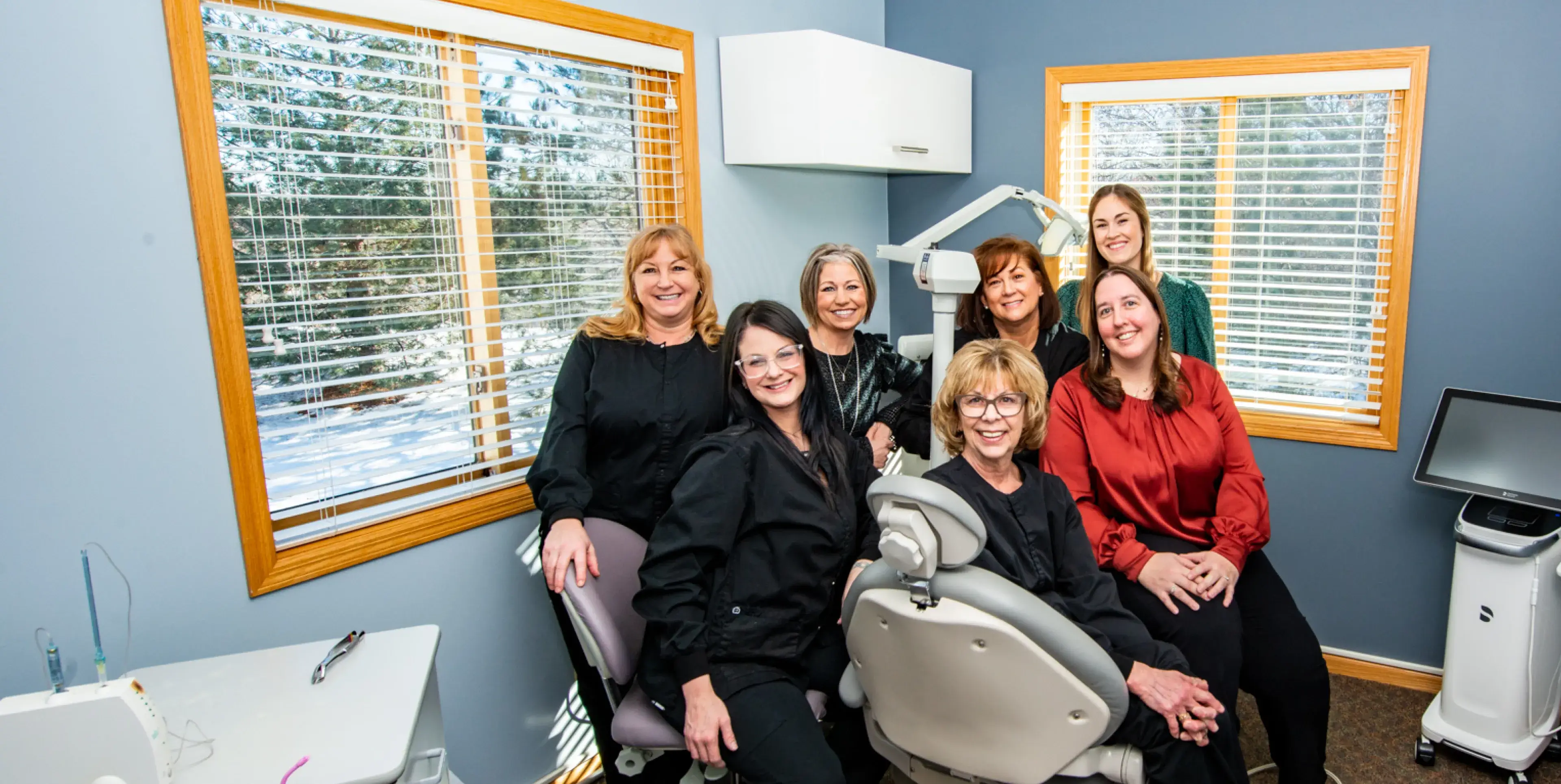 Five women in black clothing smiling in front of a framed sunset artwork on a blue wall.