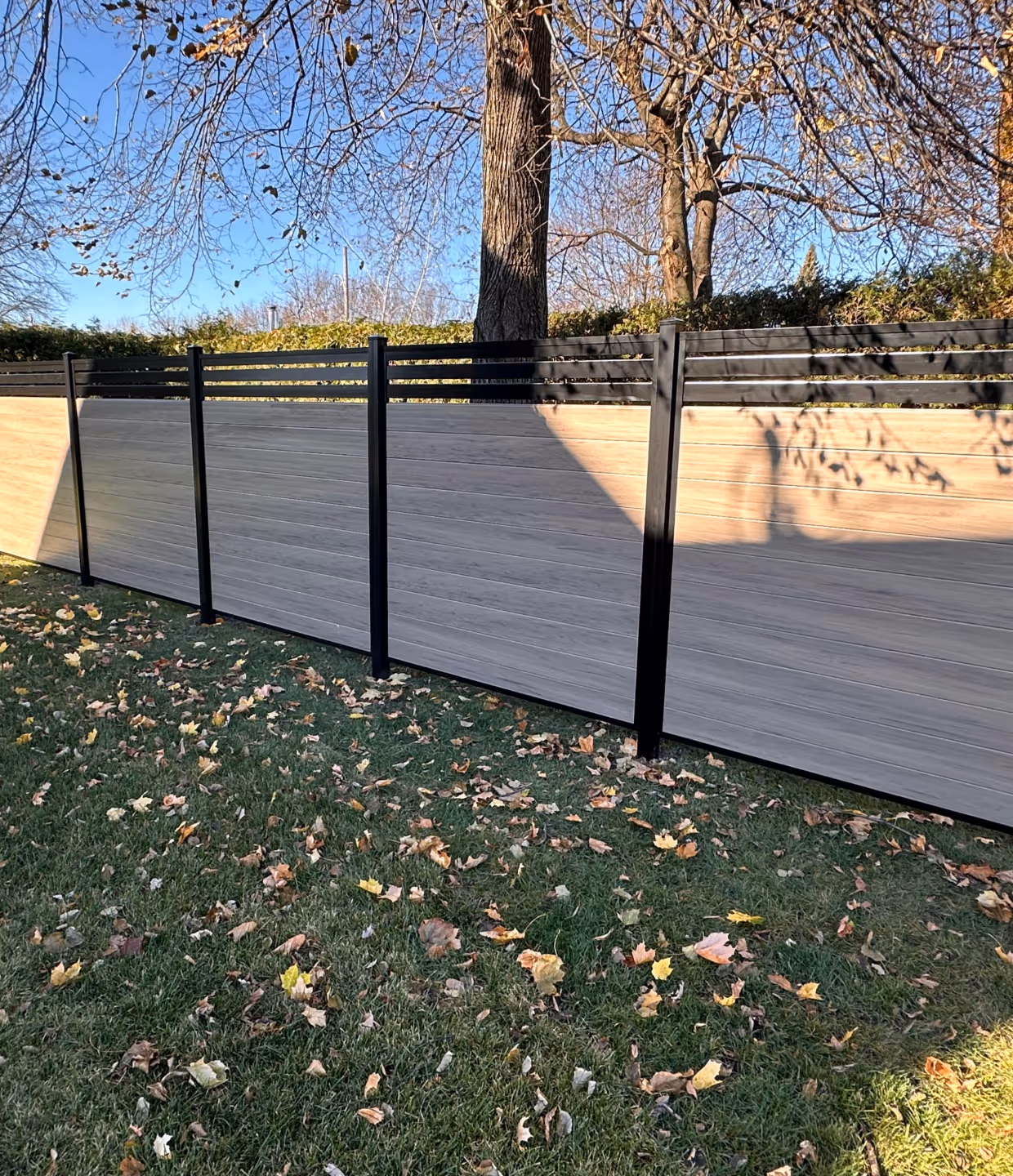 Clôture d'intimité en PVC gris pâle avec une section supérieure ajourée, installée dans une cour en automne.