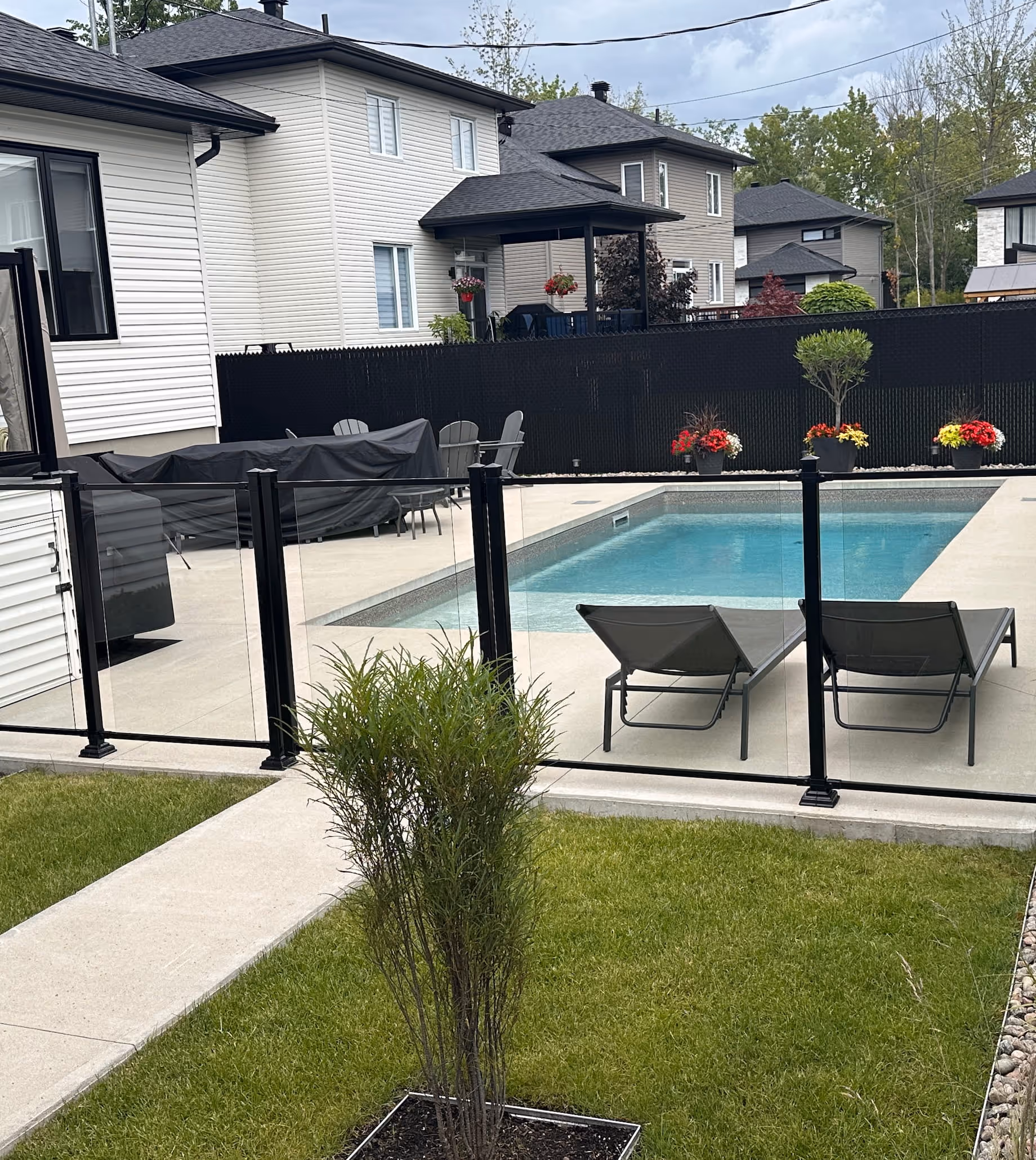Cour avec piscine, sécurisée par une clôture en verre et une clôture en maille de chaîne avec lattes noires.