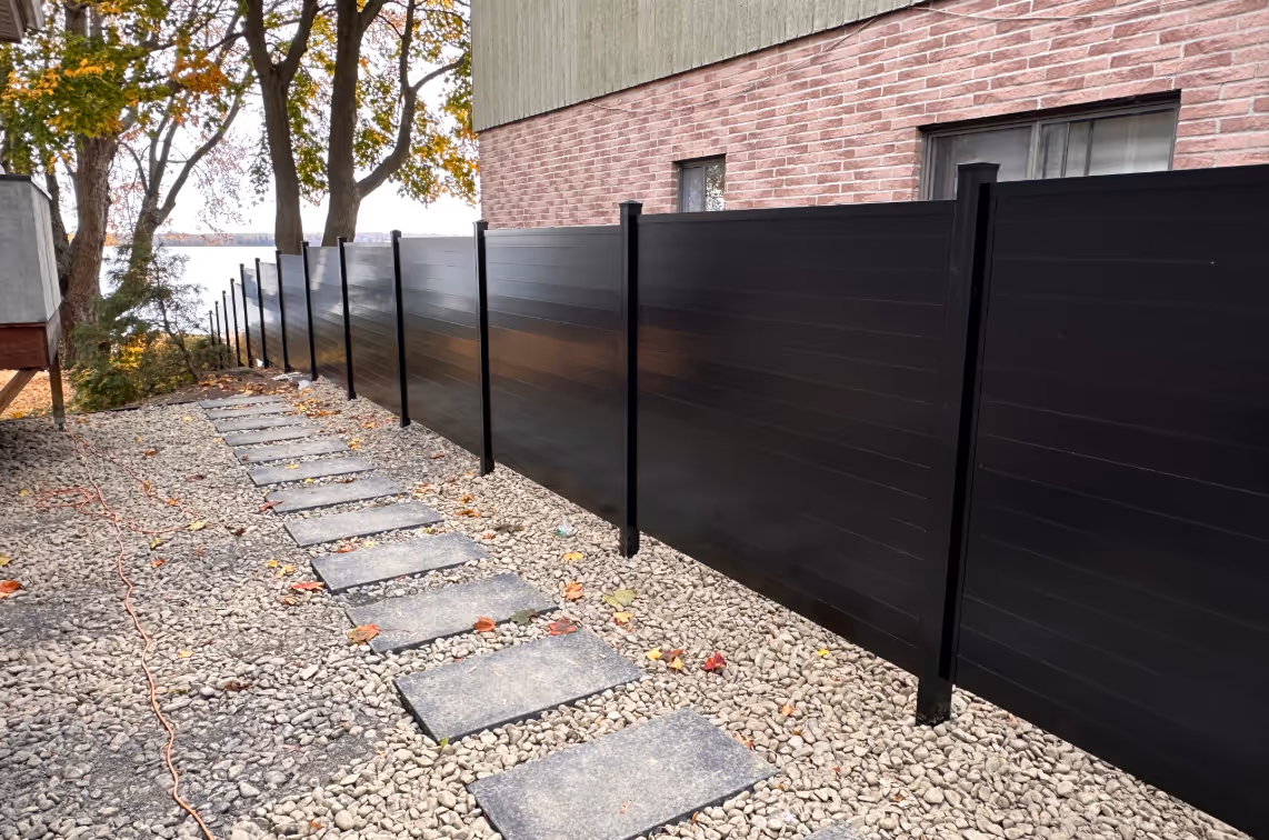 Une clôture d'intimité en aluminium noire adjacente à un mur en briques.