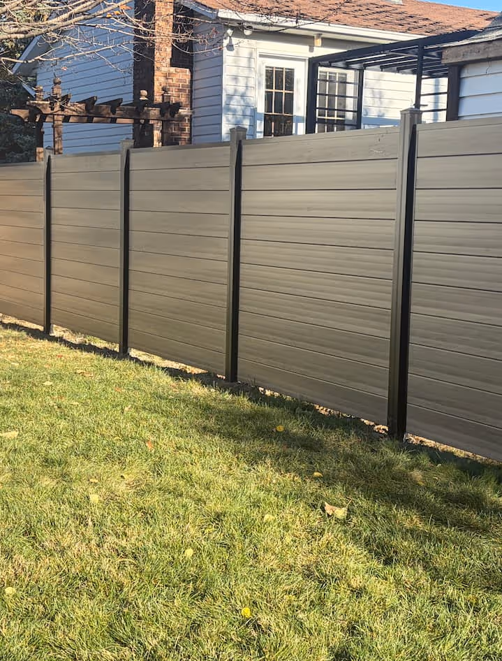 Clôture contemporaine PVC taupe avec des panneaux horizontaux devant une maison blanche avec porte-fenêtre et pelouse verte.