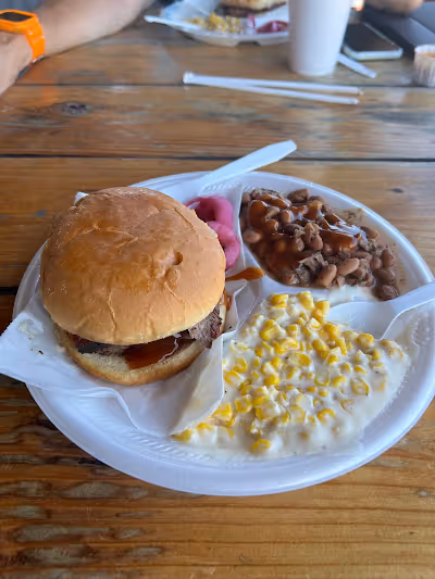 A plate featuring a hamburger alongside servings of beans and corn.