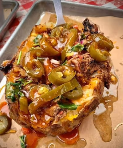A baked potato topped with seasoned meat and colorful bell peppers, served on a white plate.