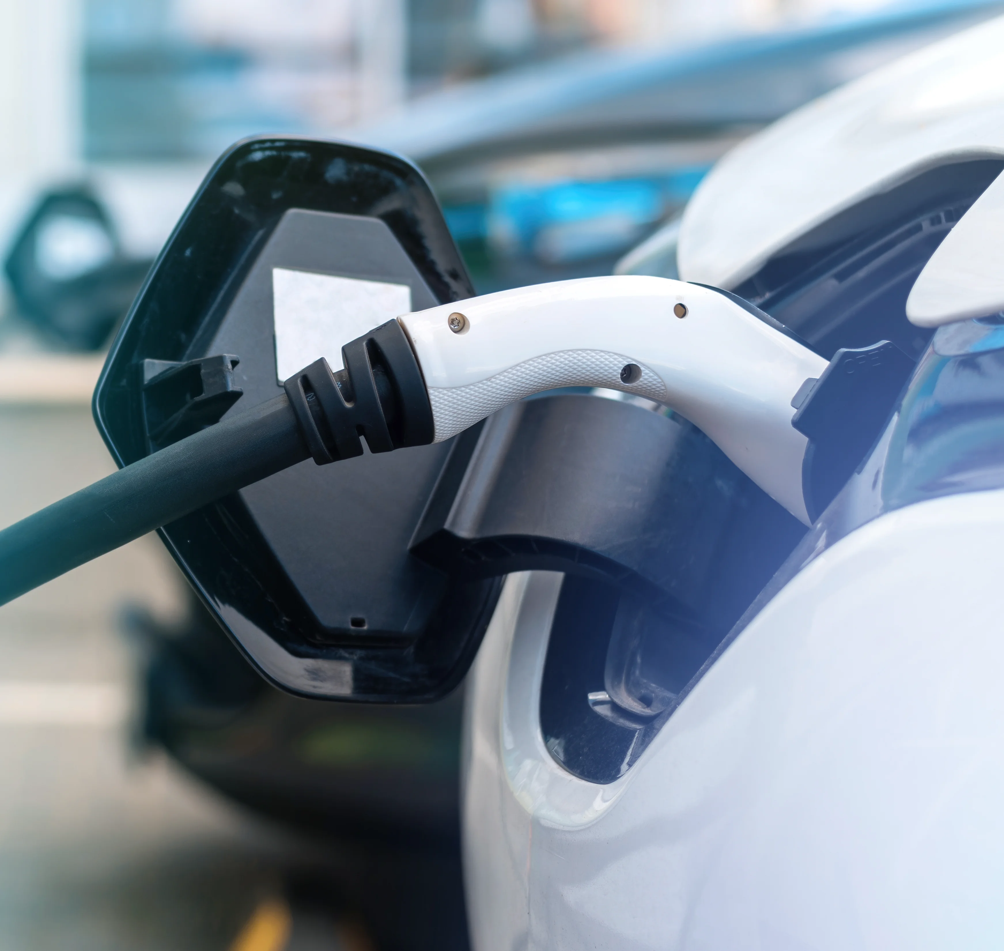 Close-up of a white electric vehicle charging plug connected to a car's charging port.