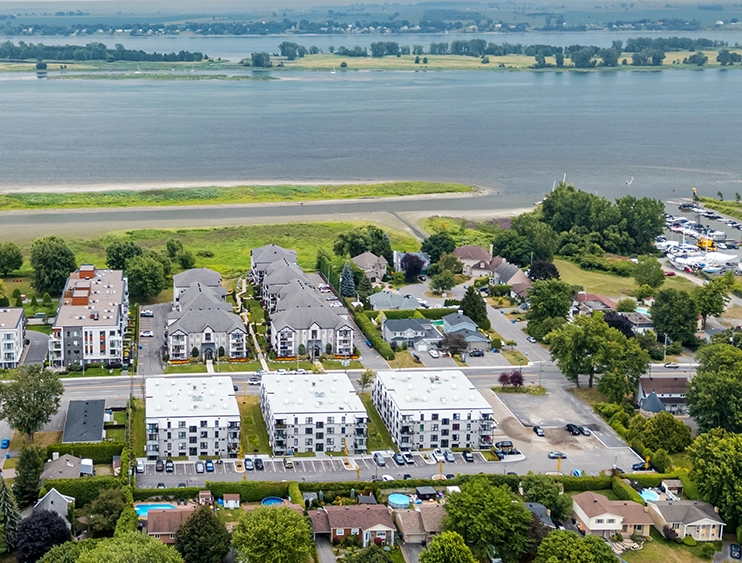Aerial view of a residential neighborhood next to a river with apartment buildings, houses, trees, and parked cars.