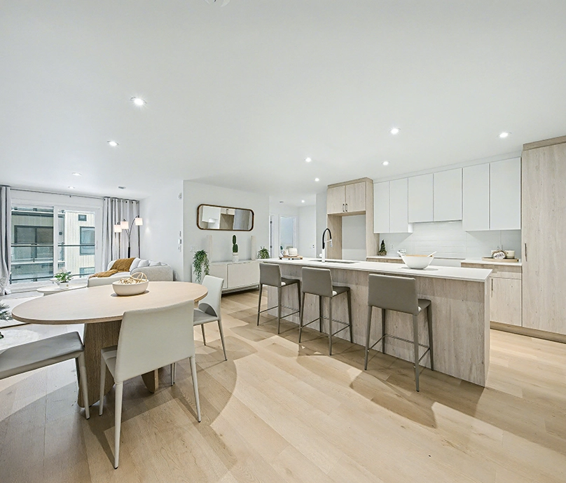 Modern open kitchen and dining area with light wood flooring, a large island with three stools, and a round dining table surrounded by chairs.