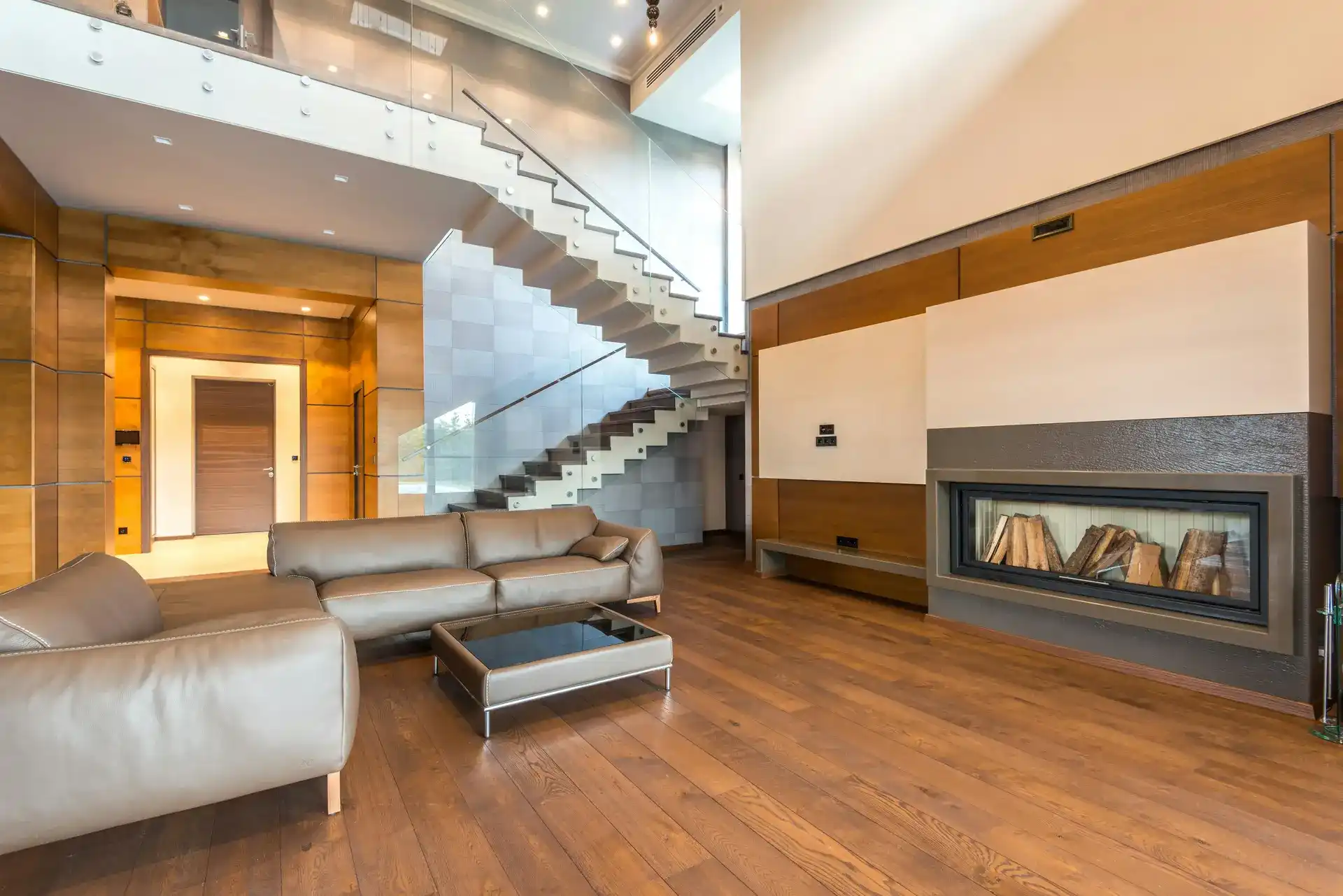 Modern living room with wooden flooring, custom fireplace design, and open staircase with glass railing