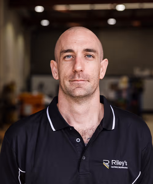 Head-and-shoulders portrait of a smiling male technician in a workshop polo