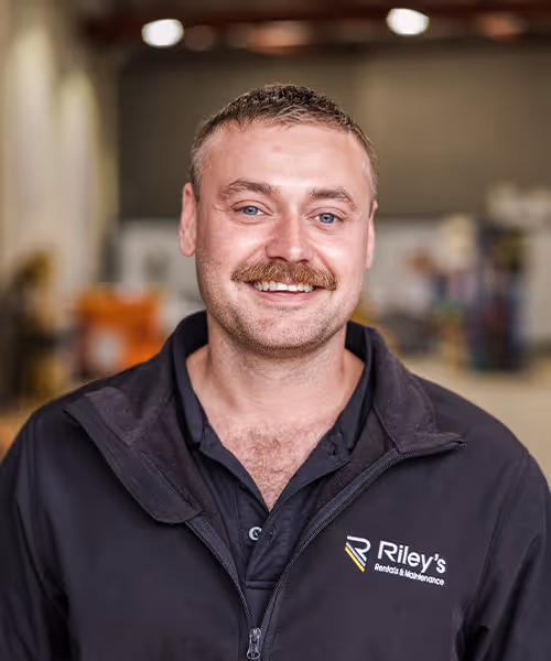 Head-and-shoulders portrait of a smiling male technician in a workshop polo