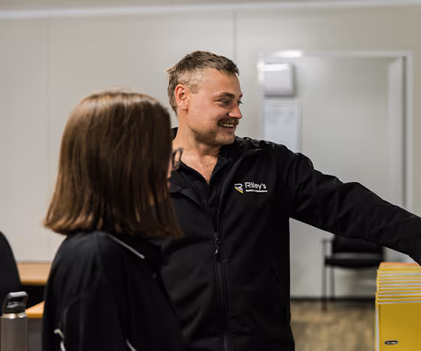 Two workers in high-visibility and black polos discussing in a workshop