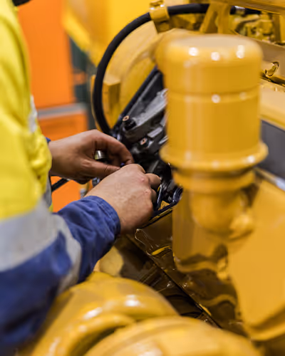 Close-up of a technician’s hands adjusting a yellow engine valve in a workshop
