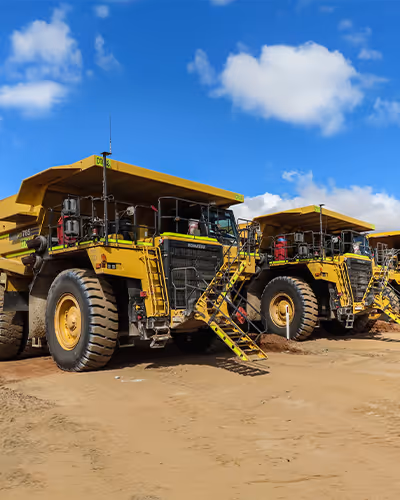 Line of yellow dump trucks parked outdoors beneath a clear blue sky
