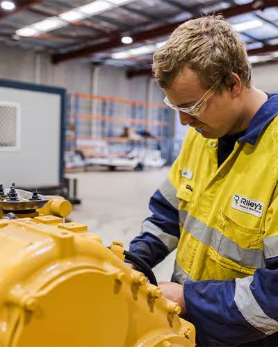 Technician in high-visibility workwear examining machinery inside an industrial workshop
