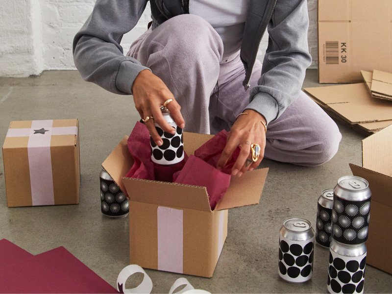 Person packing patterned drink cans into gift boxes